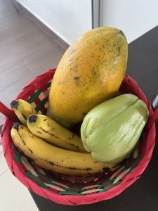 A colorful woven basket filled with ripe papaya, spotted yellow bananas, and a light green chayote.