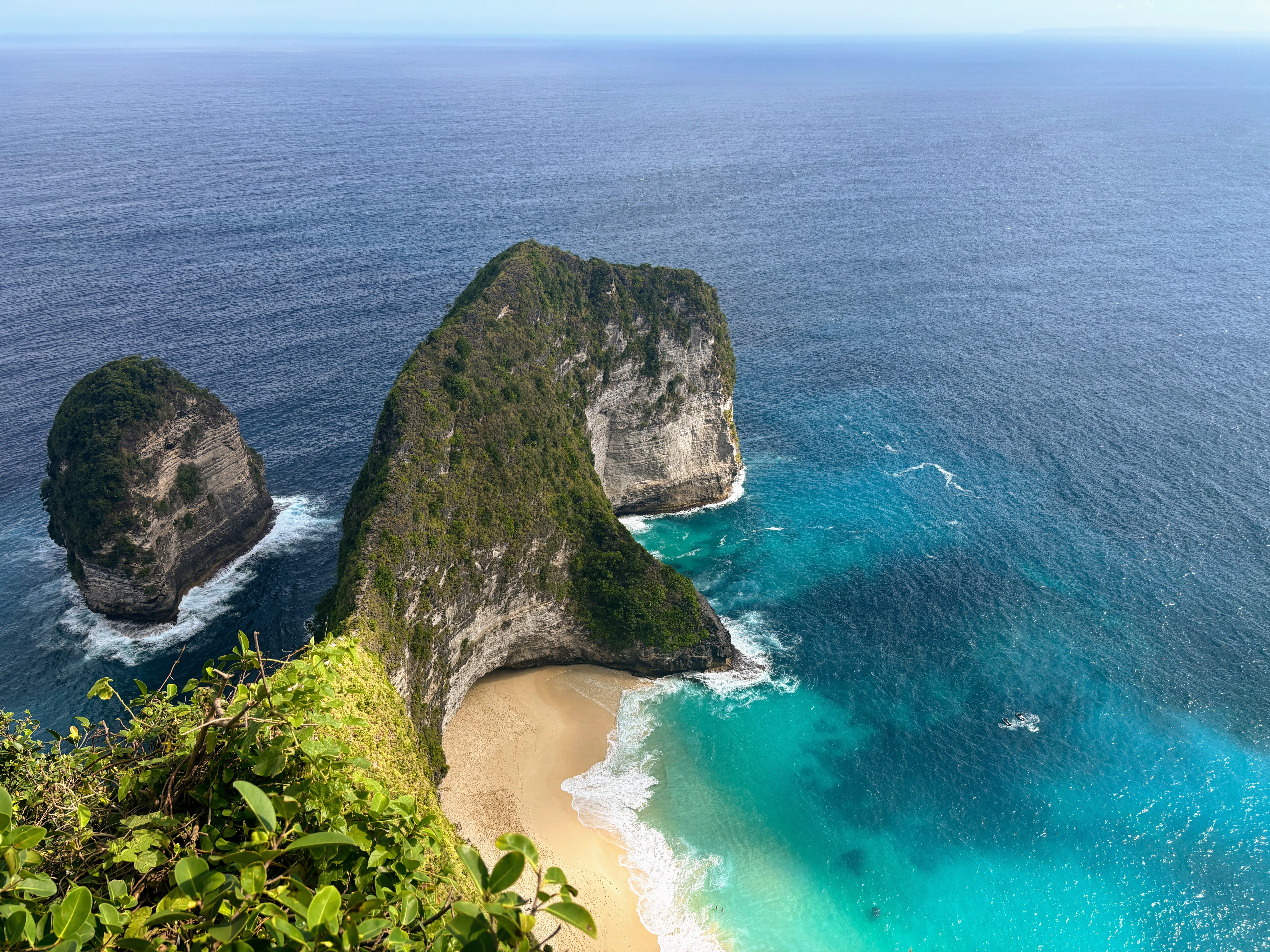 Nusa Penida beach with turquoise water, green cliffs, and a rocky islet offshore.