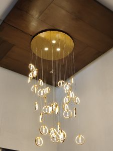 A modern ceiling light fixture hangs from a flat, wooden ceiling.