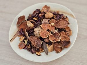 A shallow ceramic bowl filled with dried natural materials, including seed pods, nuts, bark, and dried flowers. The arrangement shows varied textures and earthy colors. Location: Feroke, Kozhikode, Kerala