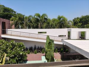 Modern white building with a sloped ramp, tropical palm trees, and landscaped garden under a clear blue sky.