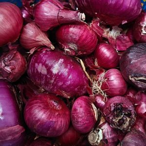 Fresh red onions piled together with purple skins and loose onion peels.
