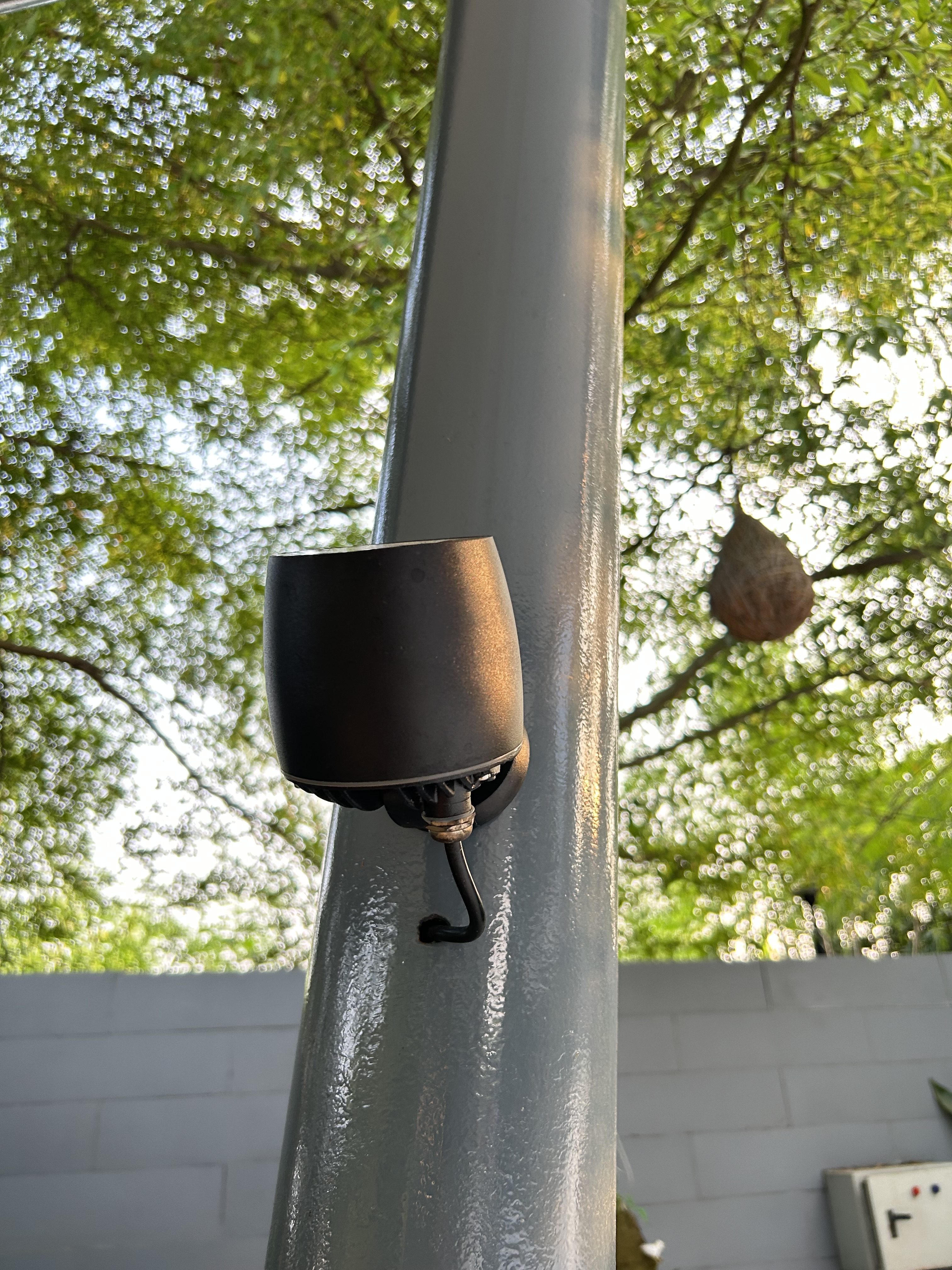 Black outdoor speaker mounted on a gray post, surrounded by green foliage.