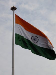 Hoisted Indian National Flag: The Indian national flag, with saffron, white and green bands and the Ashoka Chakra, billowing in the wind against a pale sky.