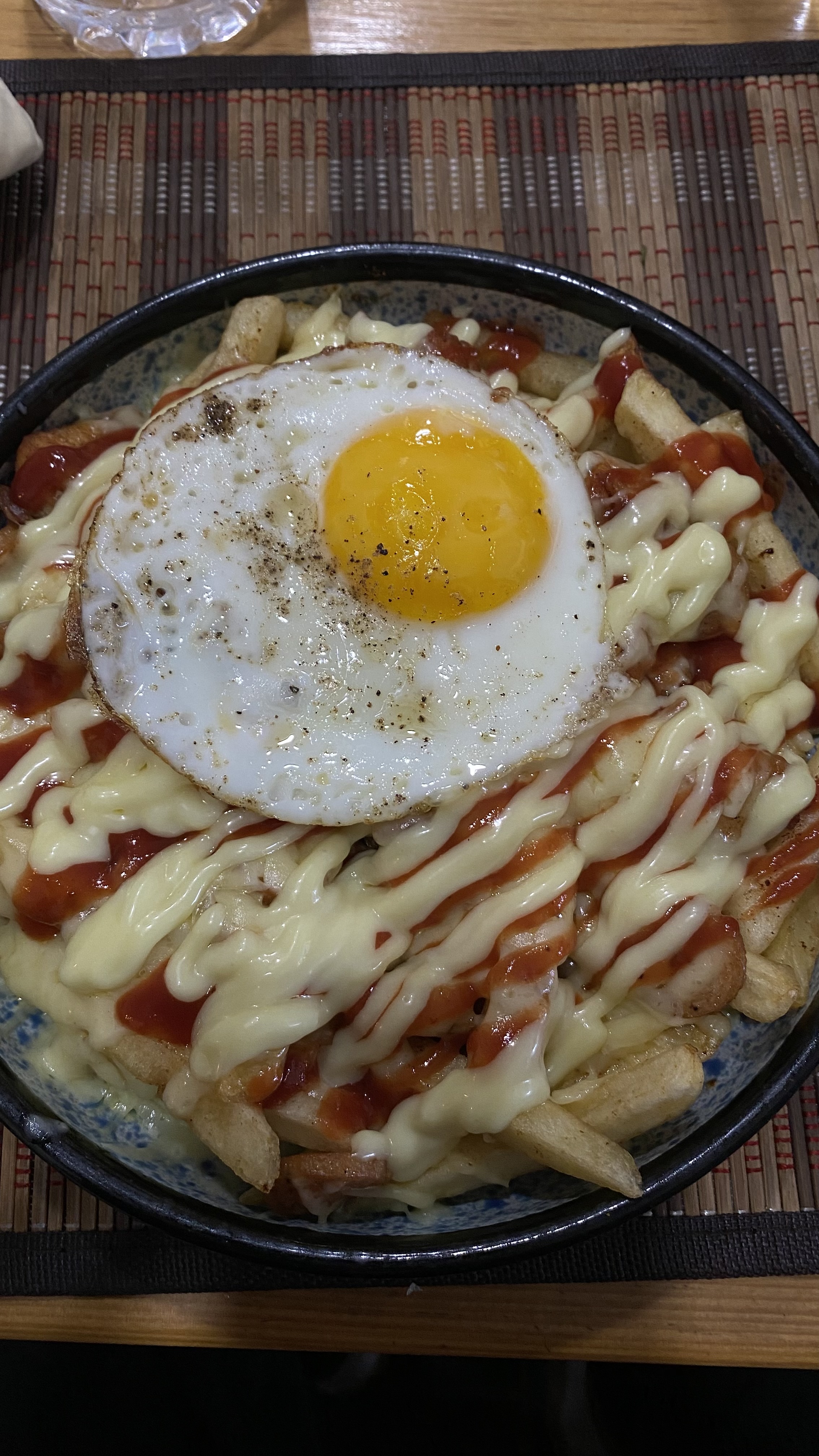 A delicious loaded bowl full of cheese, potato fries, chicken pieces, sausage, and a half fried egg at the top.