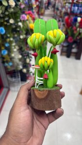 Close-up shot of a small handcrafted decorative plant figurine held in a hand, featuring a wooden base with artificial moss