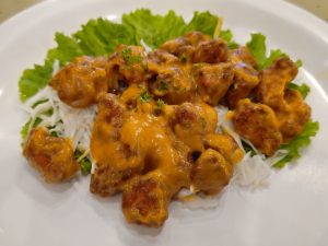 A plate of vegetables topped with golden-orange chicken pieces coated in a creamy sauce, garnished with fresh herbs and served with lettuce. The close-up highlights the food's texture and color. Location: Feroke, Kozhikode, Kerala
