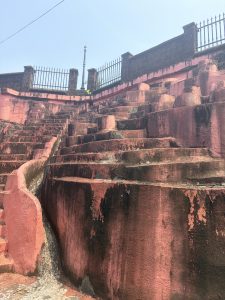 Pink stepped structure at Swami Nithyanand Ashram in Kanhangad under a bright blue sky.