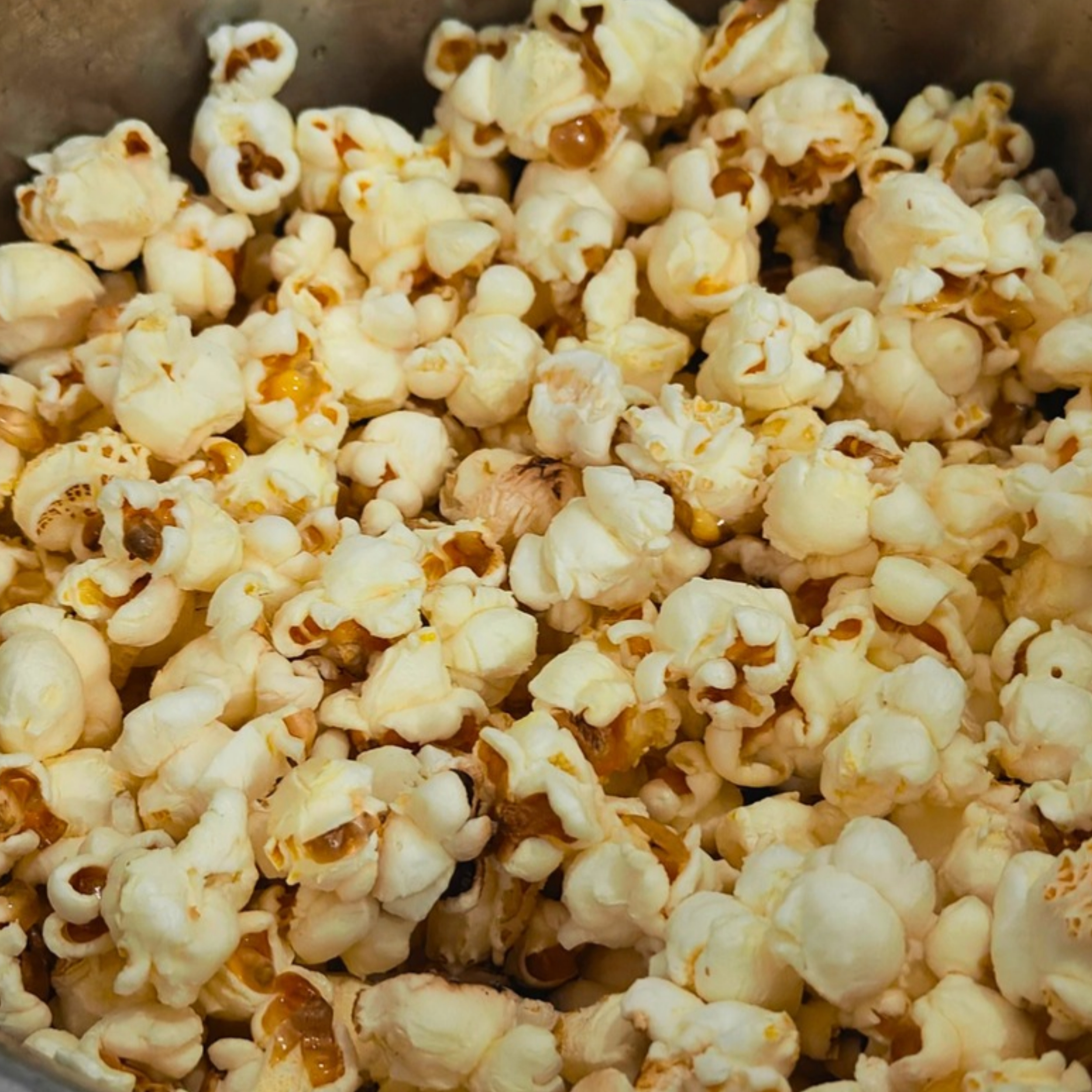 Freshly popped popcorn filling a container, with white and yellow kernels and a few toasted spots.