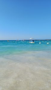 Small boats floating on clear turquoise seawater beneath a cloudless blue sky.