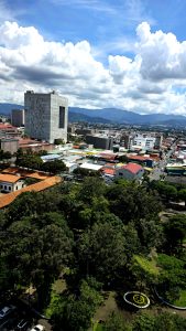 Urban landscape featuring a city park, distant mountains and dramatic cloud formations under natural daylight.
