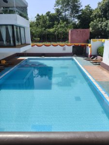 A large, rectangular outdoor swimming pool filled with clear, light-blue water, featuring tiled bottom surfaces and a shallower section or steps visible near the front left.