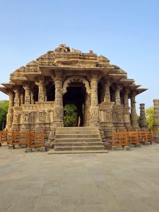 A beautiful view of the Sun Temple’s intricately carved entrance, featuring ornate stone pillars, detailed sculptures, and symmetrical architecture under a clear blue sky. Location: Sun Temple, Modhera, Mehsana district, Gujarat.
