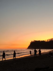 People walking on the beach at sunset with the sea on the back and a mountain
