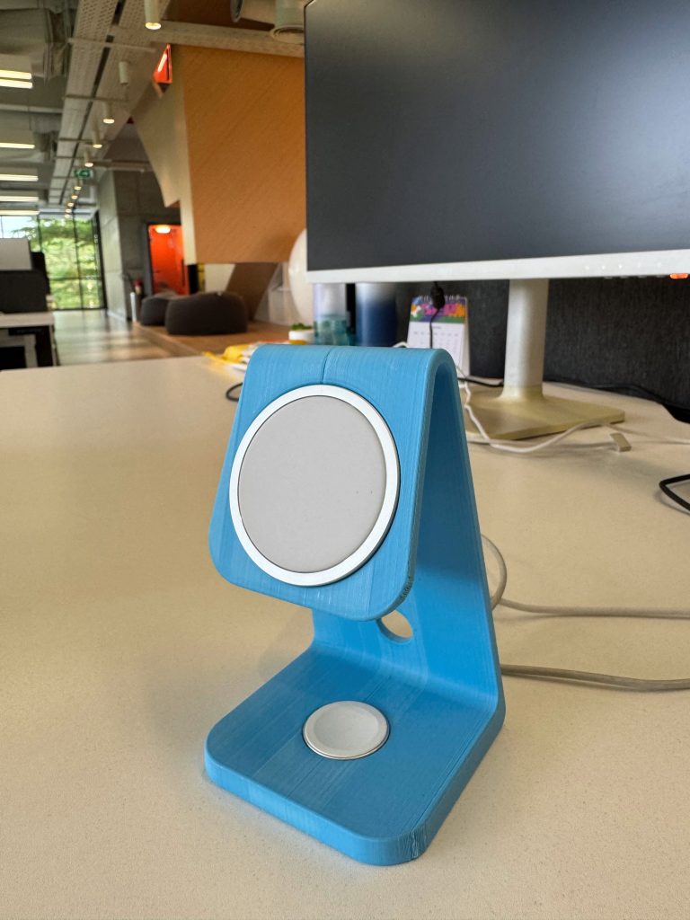3D-printed light blue MagSafe charging stand with an Apple Watch charging puck on a white office desk.