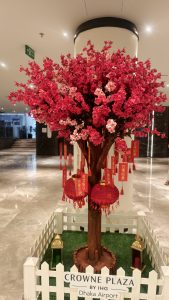 A decorative pink blossom tree decorated with red Chinese lanterns and wishing tags inside an indoor hotel lobby.