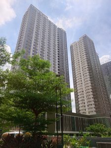 Two tall, modern grey and white high-rise tower buildings in Cebu IT Park rising behind leafy green trees under a partly cloudy sky.