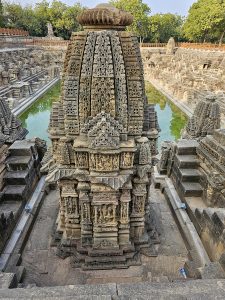 A detailed view of an ornate stone shrine, surrounded by the Sun Temple’s historic water tank and its symmetrical steps. The intricate carvings and balanced composition reveal the site’s architectural beauty. Location: Sun Temple, Modhera, Mehsana district, Gujarat.
