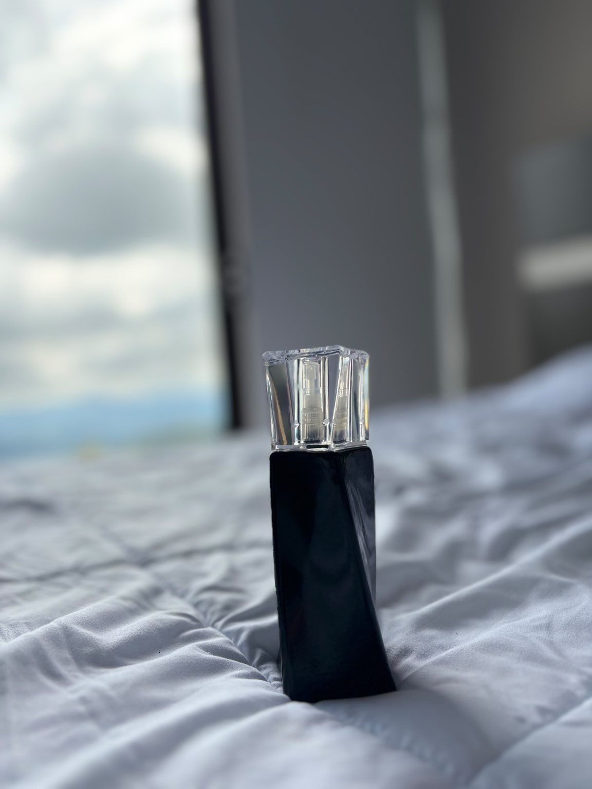 Modern perfume bottle standing on a quilted white bedspread