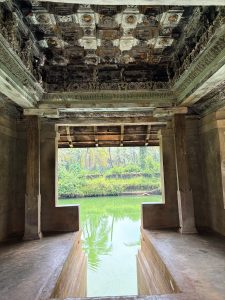 Kerala temple pavilion overlooking a green pond surrounded by palm trees.