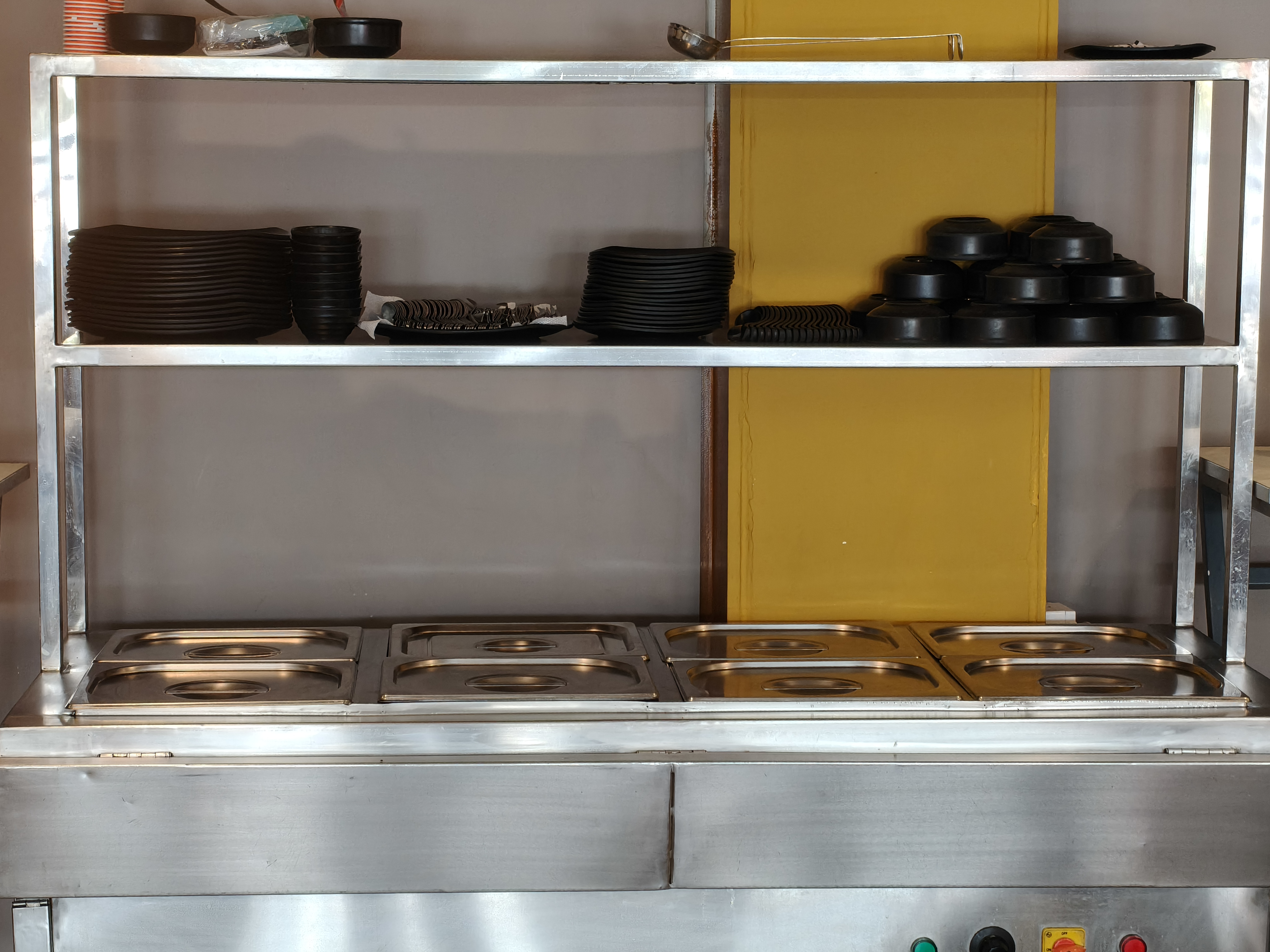 Black plates and bowls arranged on a stainless steel buffet counter above empty food trays.