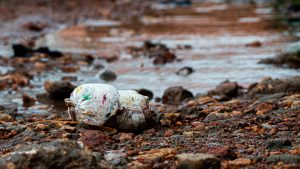 Discarded white plastic item with colorful markings in muddy, rocky ground.