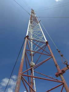 Telecommunications Tower Against Blue Sky, Low-angle view of a red and white telecommunications tower extending into a clear blue sky, highlighting the geometry and structure of the communication infrastructure.