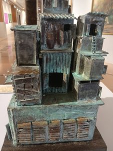 “Bronze-colored miniature model of a cluster of old industrial-style buildings displayed in a gallery. 