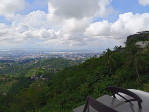 A high-altitude outdoor terrace view overlooking rolling green hills and Cebu city beneath fluffy white clouds.