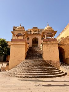 Front staircase and ornate entrance of Amer Fort in Jaipur, Rajasthan, with traditional Rajput architecture under a clear blue sky.