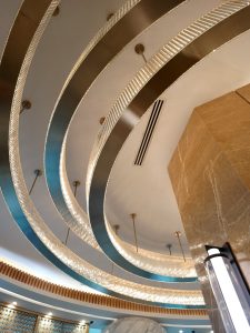A modern chandelier with concentric curved rings of sparkling crystal glass suspended from brass rods.