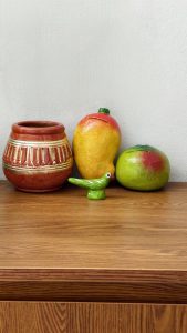Handmade clay pottery and colorful mango and parrot figurines purchased from a local fair, displayed on a wooden table.