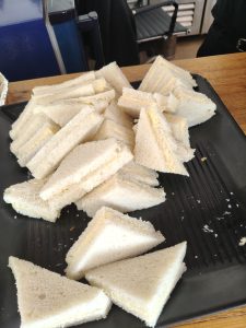 Triangular white bread sandwiches with a pale yellow filling arranged on a black serving tray.

