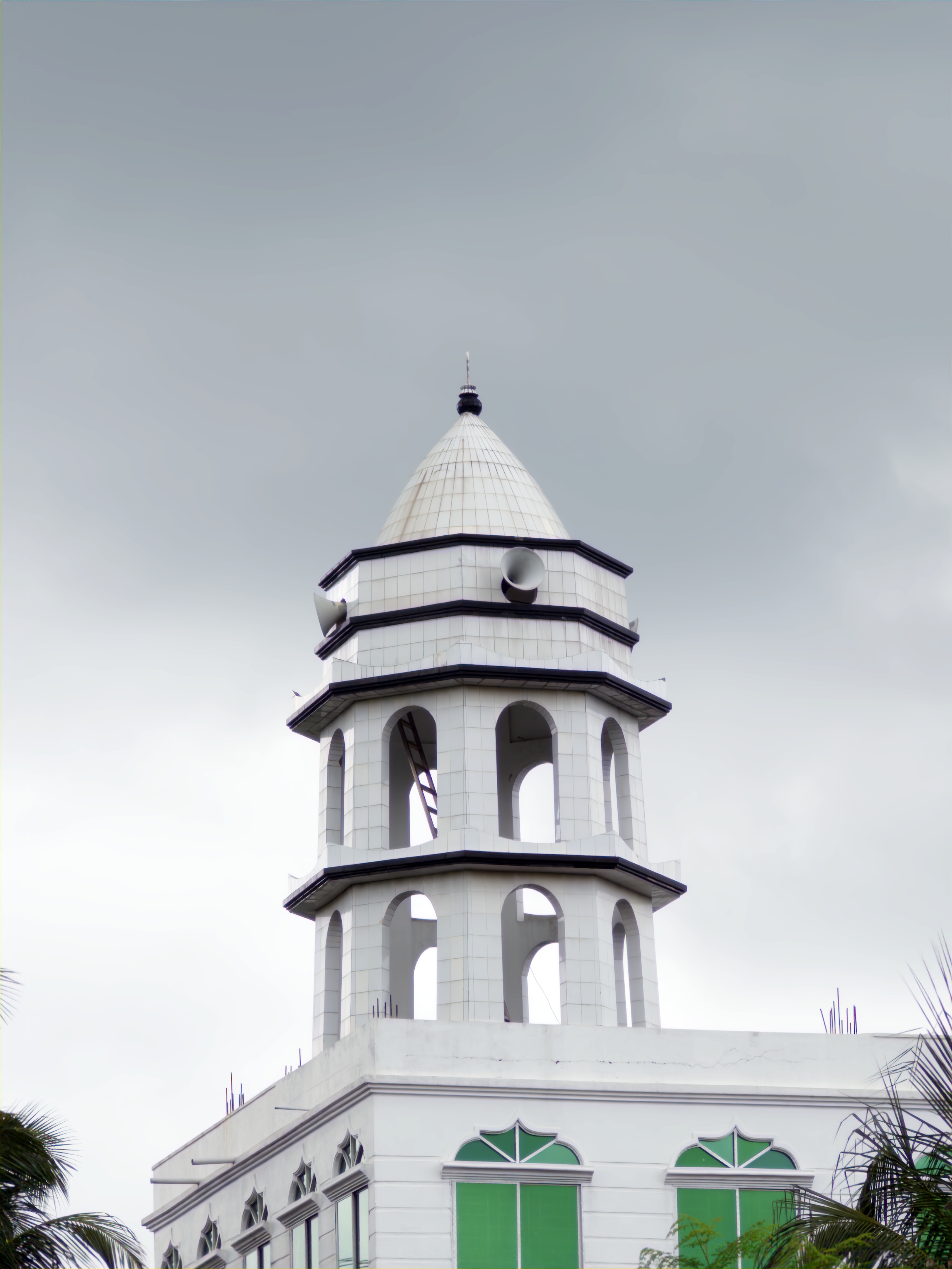 A white mosque with a tall conical dome and arched windows under an overcast sky.