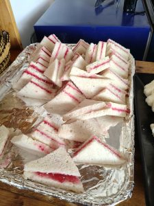 Triangular white bread sandwiches filled with red jam, arranged on a foil-lined serving tray.