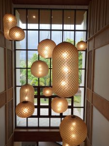 A cluster of hanging woven net pendant lanterns in spherical and oblong shapes glowing warmly in front of a tall multi-pane window.