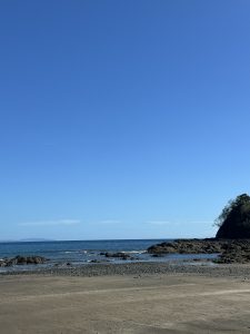 Sandy beach with blue water, rocky formations, and distant land under a clear sky.
