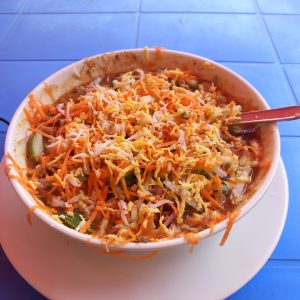 Bowl of spicy-tangy chotpoti made with spiced peas and potatoes, topped with grated boiled egg, shredded carrot, cucumber and onion.