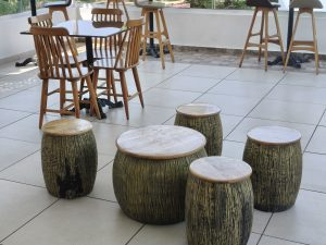 Rustic barrel-shaped wooden stools and a matching round table arranged in a modern café with wooden chairs and tables.