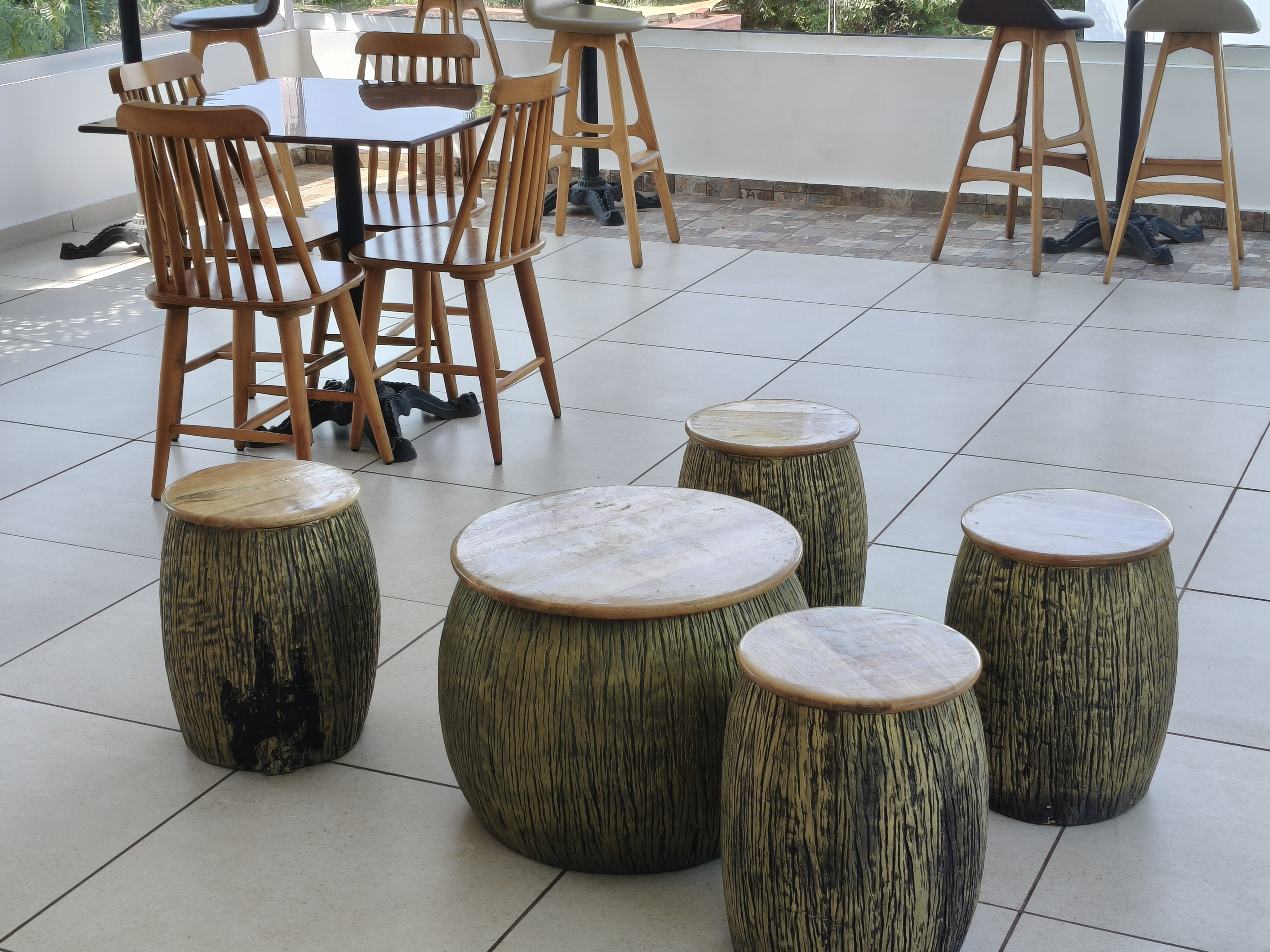 Rustic barrel-shaped wooden stools and a matching round table arranged in a modern café with wooden chairs and tables.