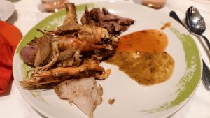 A round plate served with grilled prawns, barbecue meat pieces, and fish fillet placed next to chili sauce and green herb dip.
