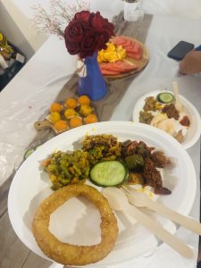 A famouse nepali food ‘selroti’ served with different varieties of chicken dishes in a white plate. The background consists of sweets, salad platter and a vase with red roses.