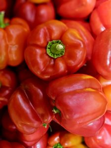 A close-up of fresh red bell peppers (Capsicum) piled together, with a prominent green stem in the center. The vibrant red color and natural textures create an attractive market photograph. Taken at Palazhi, Kozhikode, Kerala.
