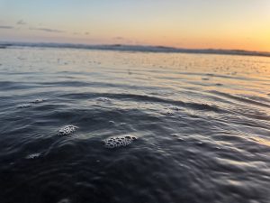 Gentle waves washing onto a sandy beach at sunset, reflecting warm orange colors in the water.