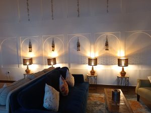 Four glowing brass table lamps with perforated lattice shades set on side tables behind a dark blue upholstered sofa.