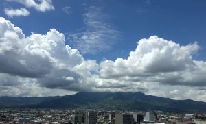 San José Skyline Beneath Mountain Clouds, Panoramic view of San José, Costa Rica, with the city skyline, surrounding mountains, and dramatic cloud formations rising above the Central Valley