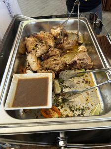 Roast chicken pieces in a buffet tray with lime wedges, vegetables, and a small dish of brown gravy. 