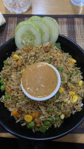 A delicious bowl of fried rice with mixed vegetables, served with special sauce and cucumber. 