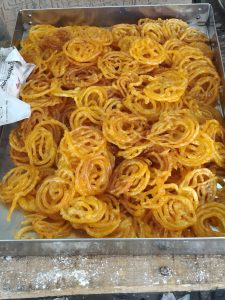 A metal tray filled with golden-orange jalebi sweets soaked in syrup.
